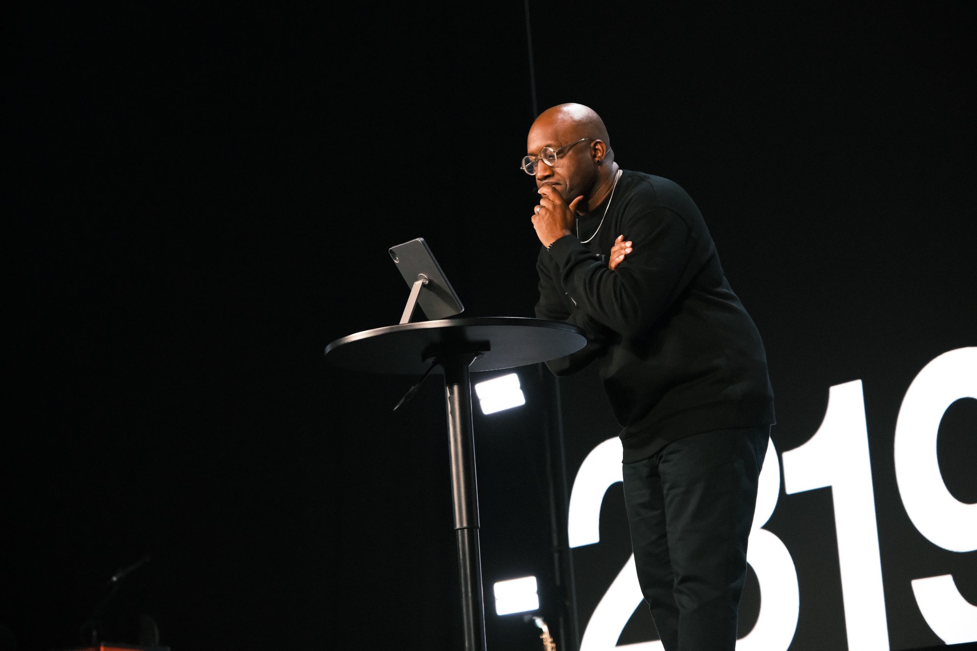 Lonnell Williams at podium on stage, hand on chin, deep in thought at 2819 Church