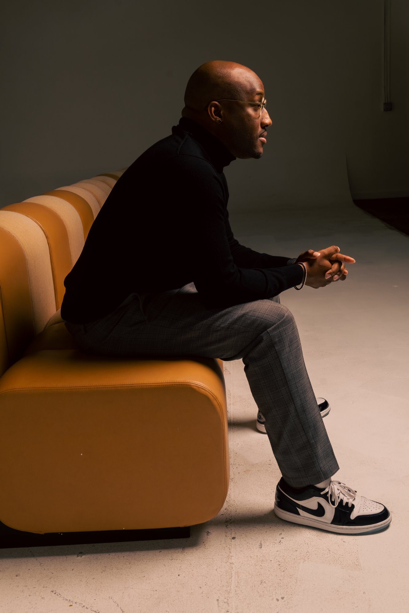 Lonnell Williams seated profile on leather couch, contemplative side view against white studio cyclorama wall